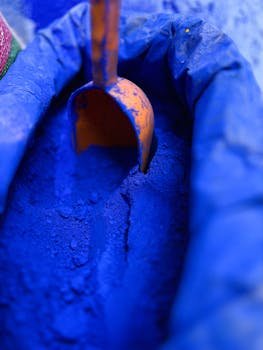 Close-up of a vivid blue pigment with an orange scooper inside a sack, offering a vibrant color display.