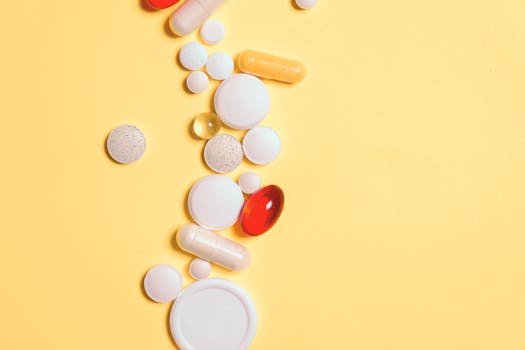 A collection of assorted pills and capsules on a vibrant yellow surface.