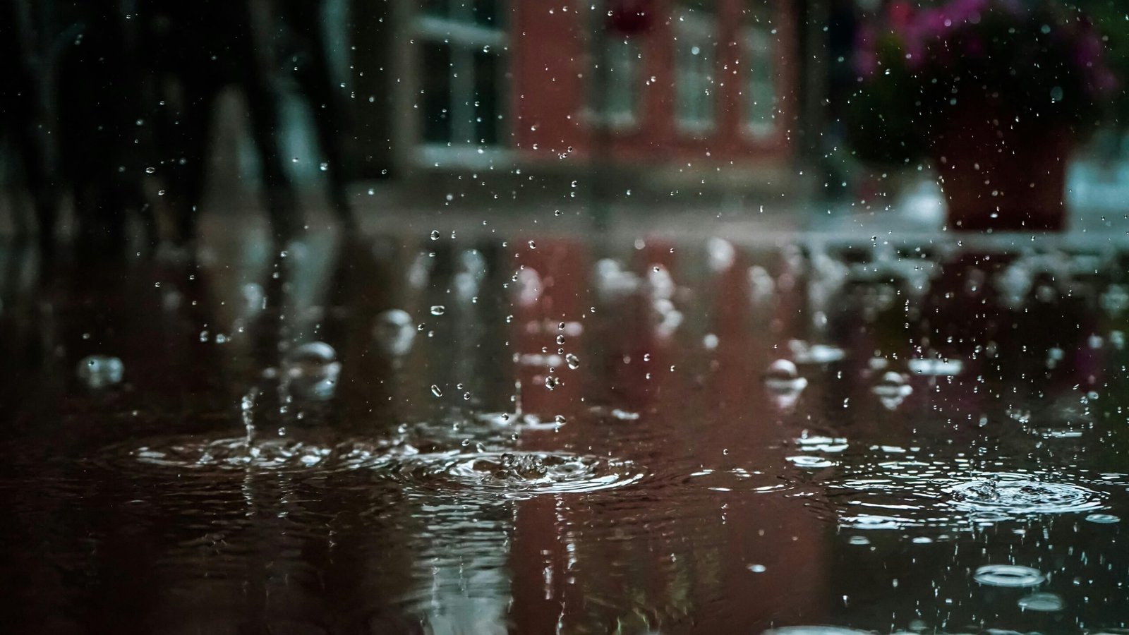 About Us Close-up of raindrops splashing into a puddle, capturing reflections and textures in an outdoor urban setting.
